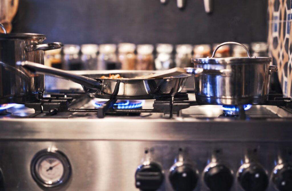Stainless steel pots and pans on a gas stove with blue flames — best cookware for gas stoves