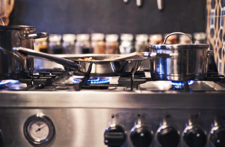 Stainless steel pots and pans on a gas stove with blue flames visible — best cookware for gas stoves