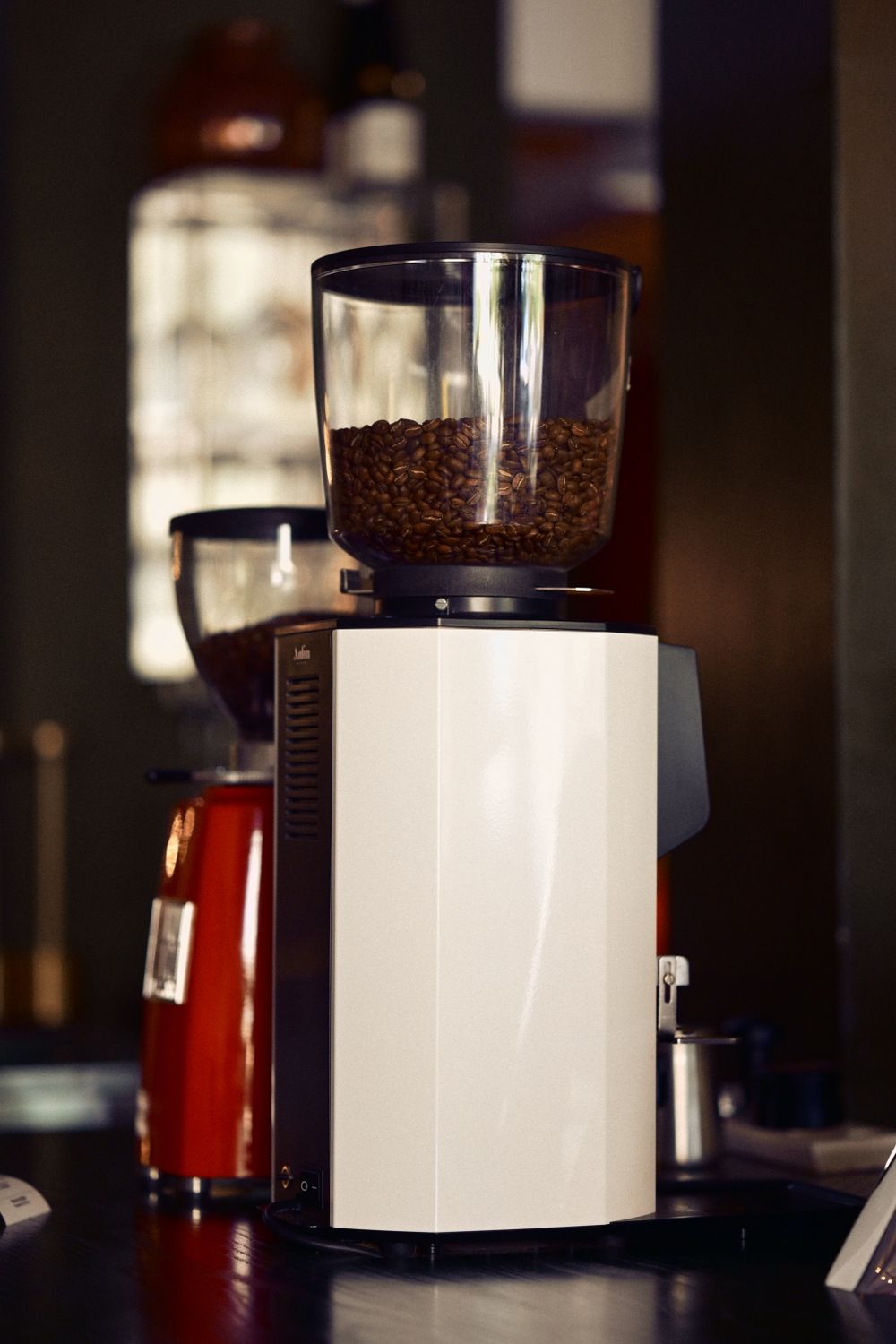 A sleek coffee grinder filled with beans on a cafe counter