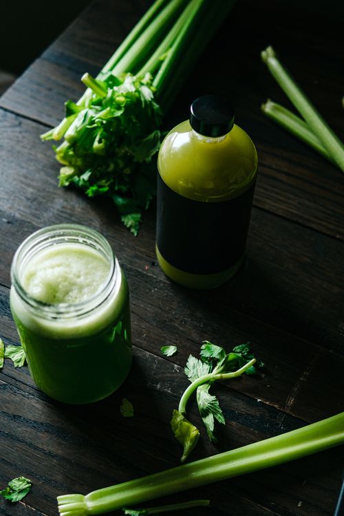 Glass of fresh green celery juice with celery stalks on a wooden surface