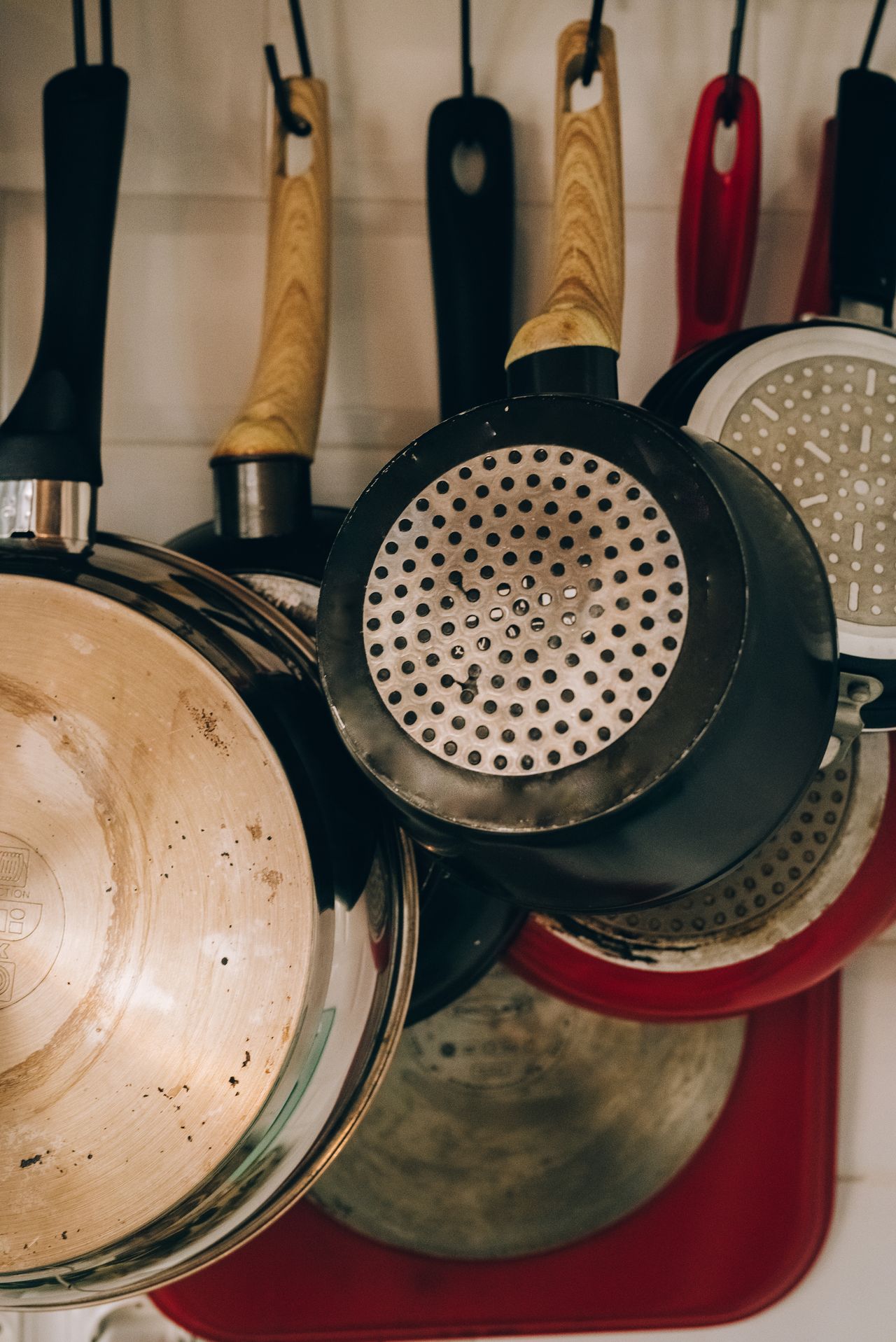 A collection of metal frying pans with wooden handles hanging in a kitchen