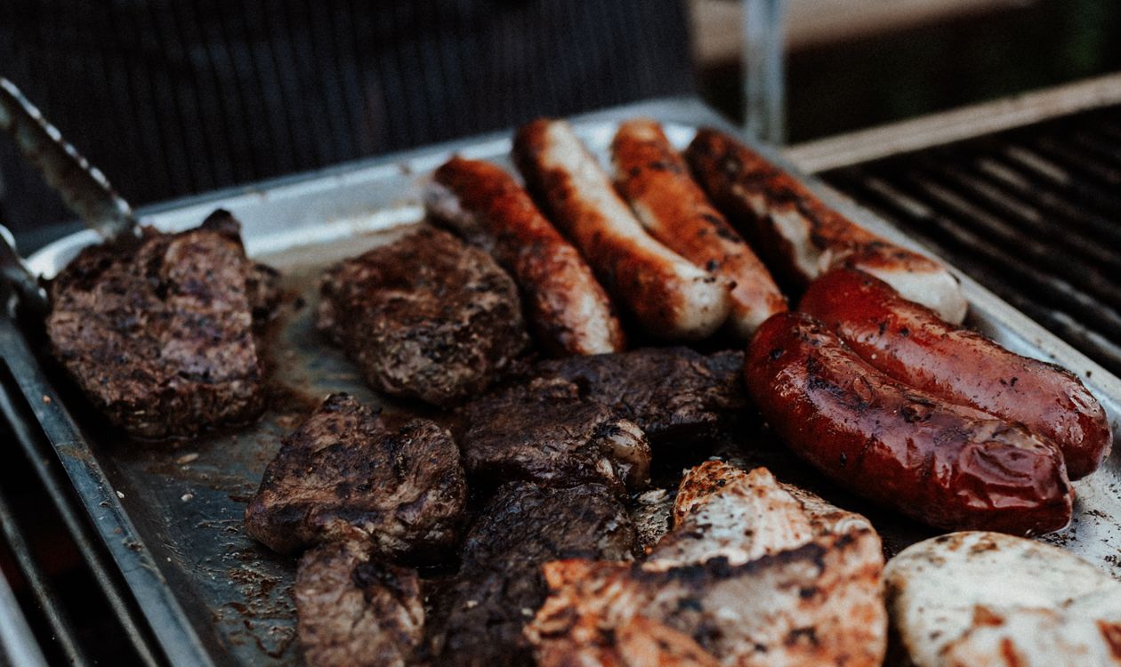 Assorted meats grilling on a barbecue for a meat temperature guide