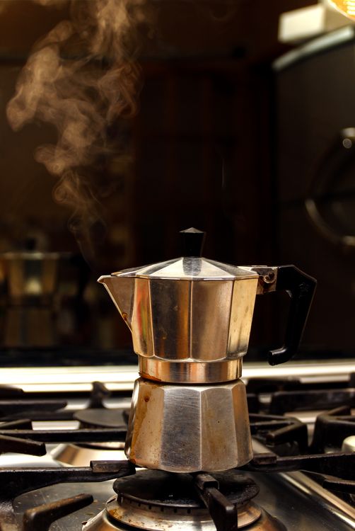 Classic moka pot steaming on a gas stove, brewing espresso coffee