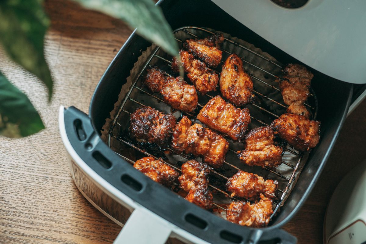 Air fryer basket pulled out with cooked chicken pieces inside, on a kitchen worktop