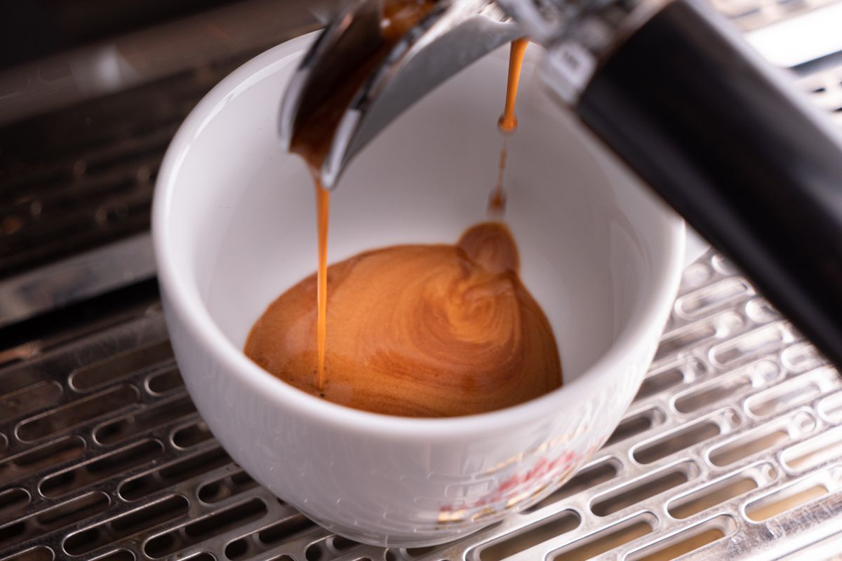 Espresso pouring from a portafilter into a white cup, showing a thick layer of crema