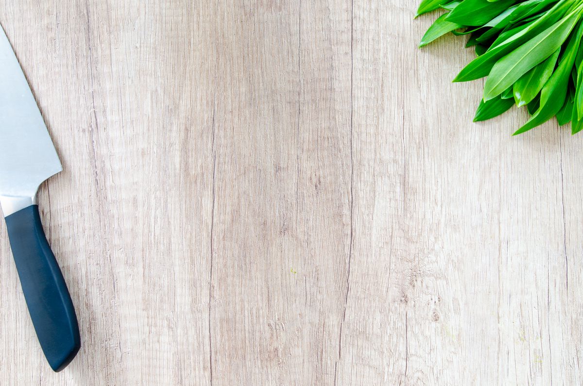 Chef’s knife lying on a light wooden board next to fresh herbs