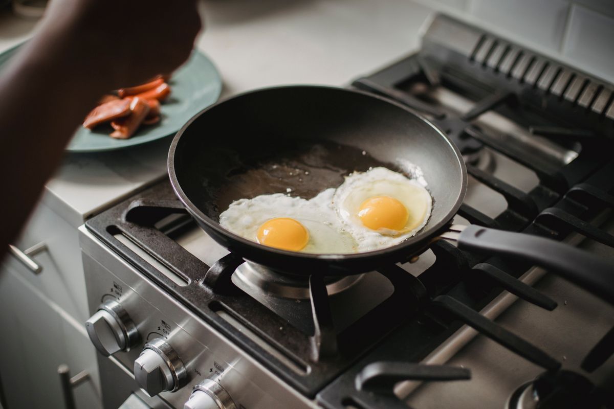 Two eggs frying in a dark non-stick frying pan on a gas hob, cooked with barely any visible fat