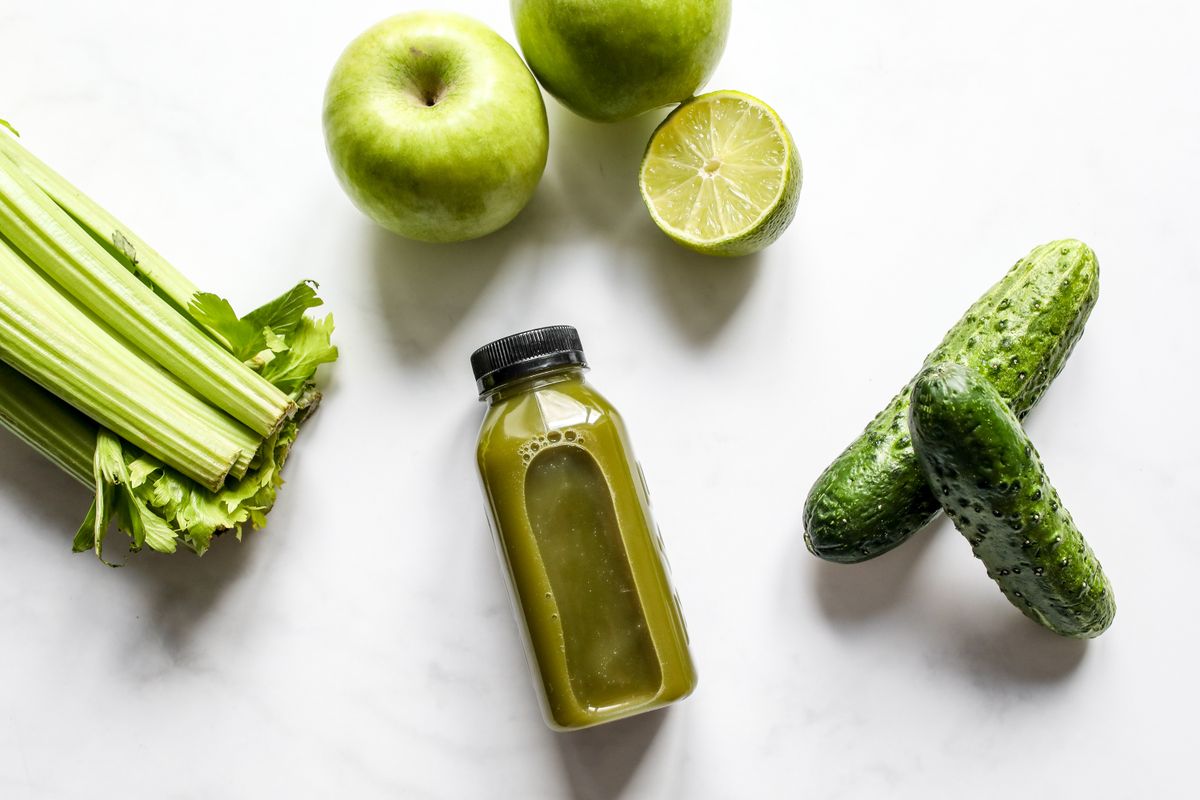 Freshly extracted green vegetable juice with celery and produce on a counter