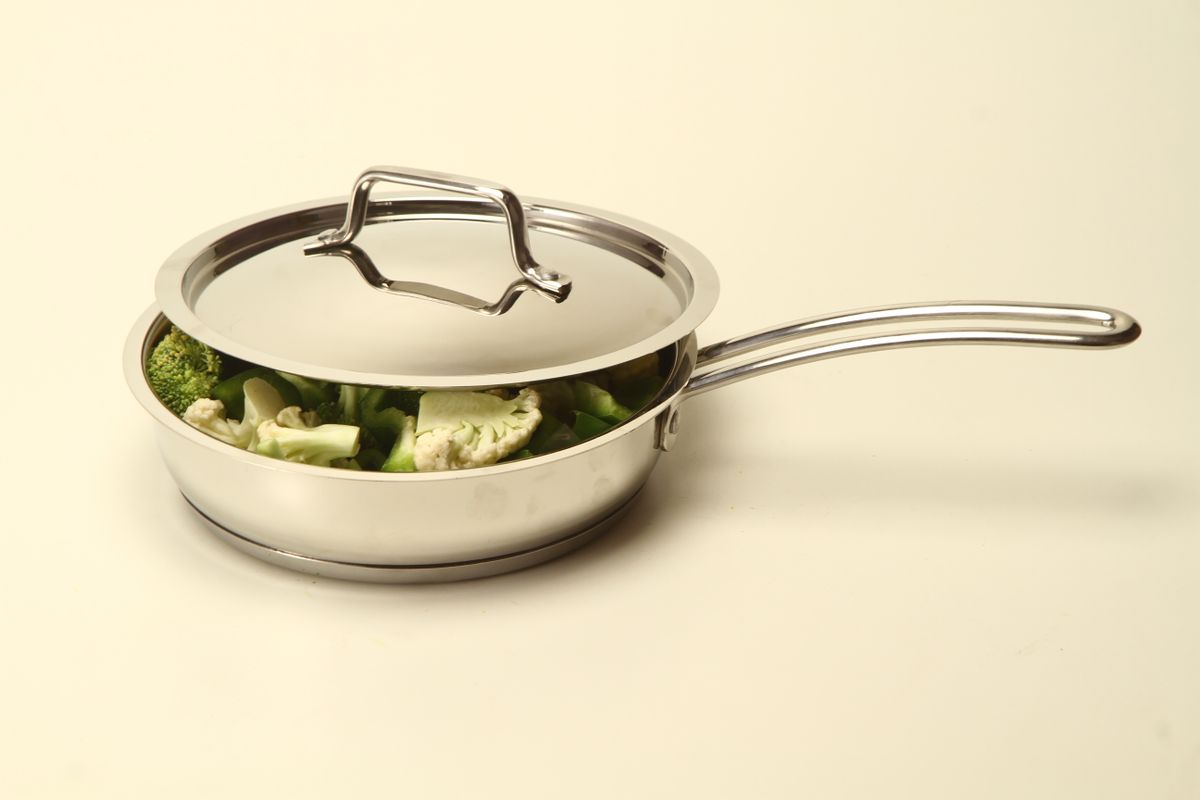 Bare stainless steel pan with a lid and vegetables, showing the bright uncoated cooking surface