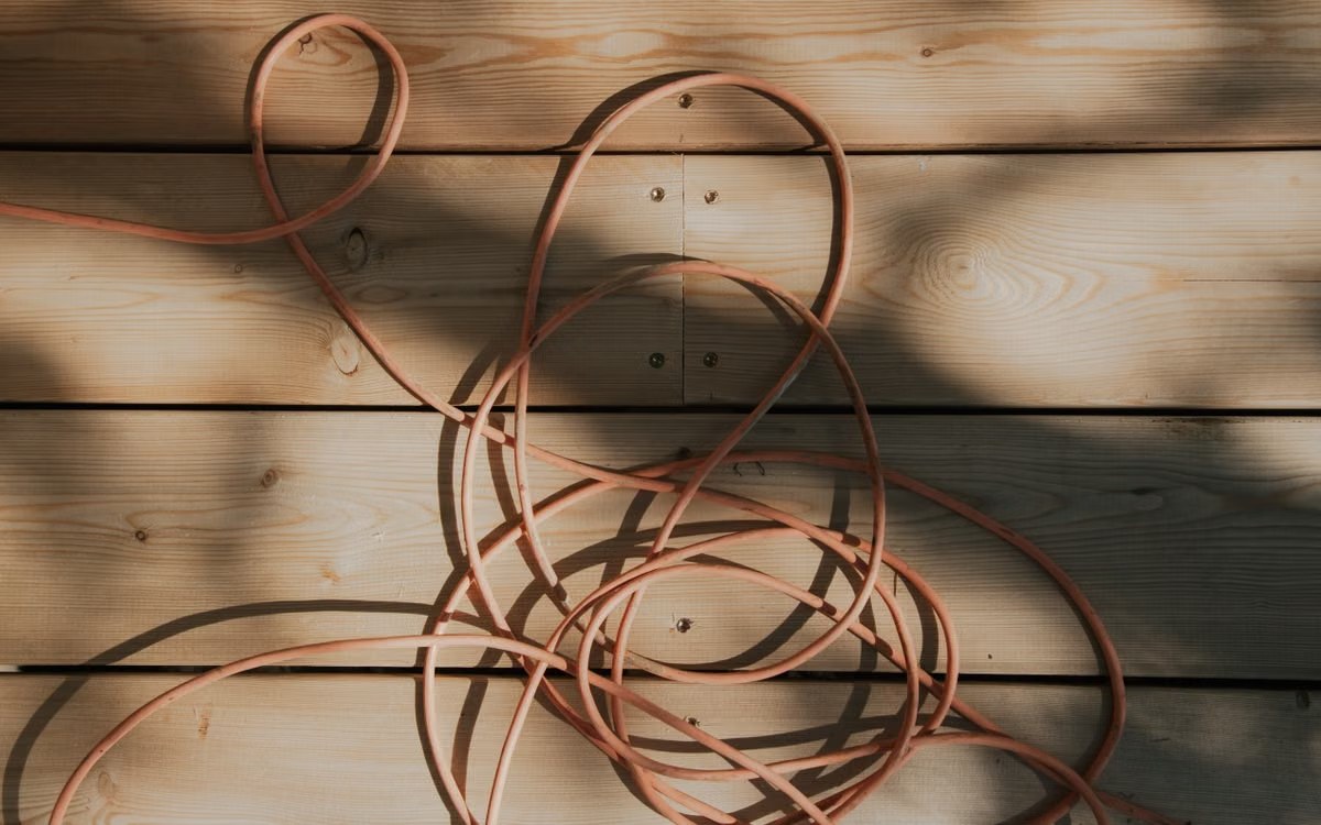 Orange outdoor extension cord coiled loosely on a sunlit wooden deck