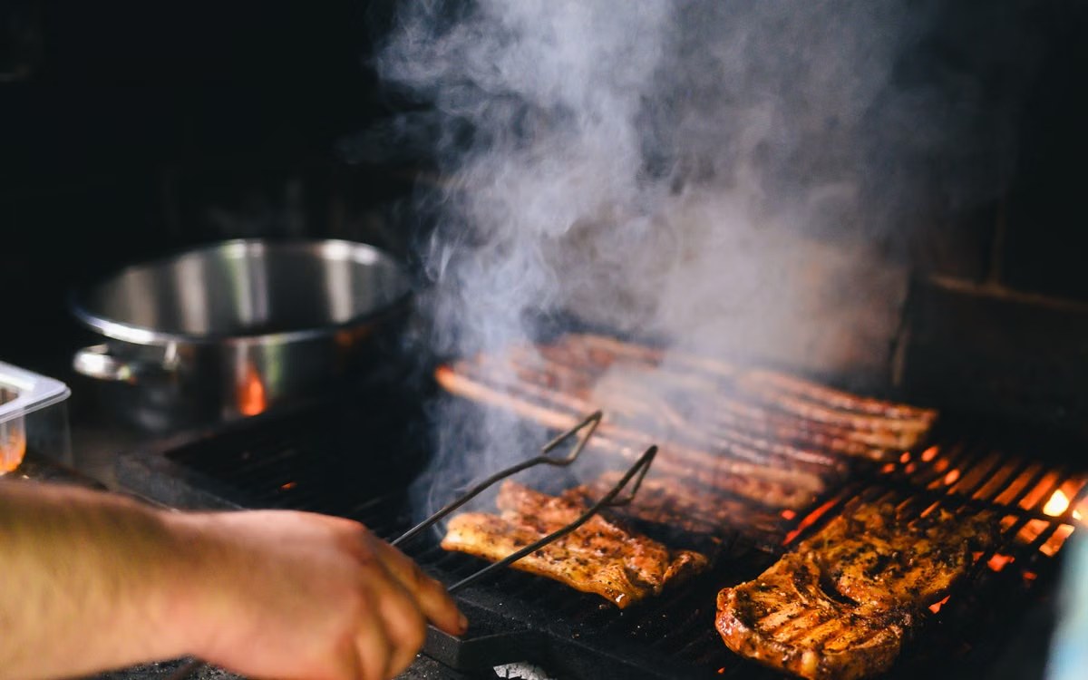 Smoke rising over racks of meat on a barbecue grate