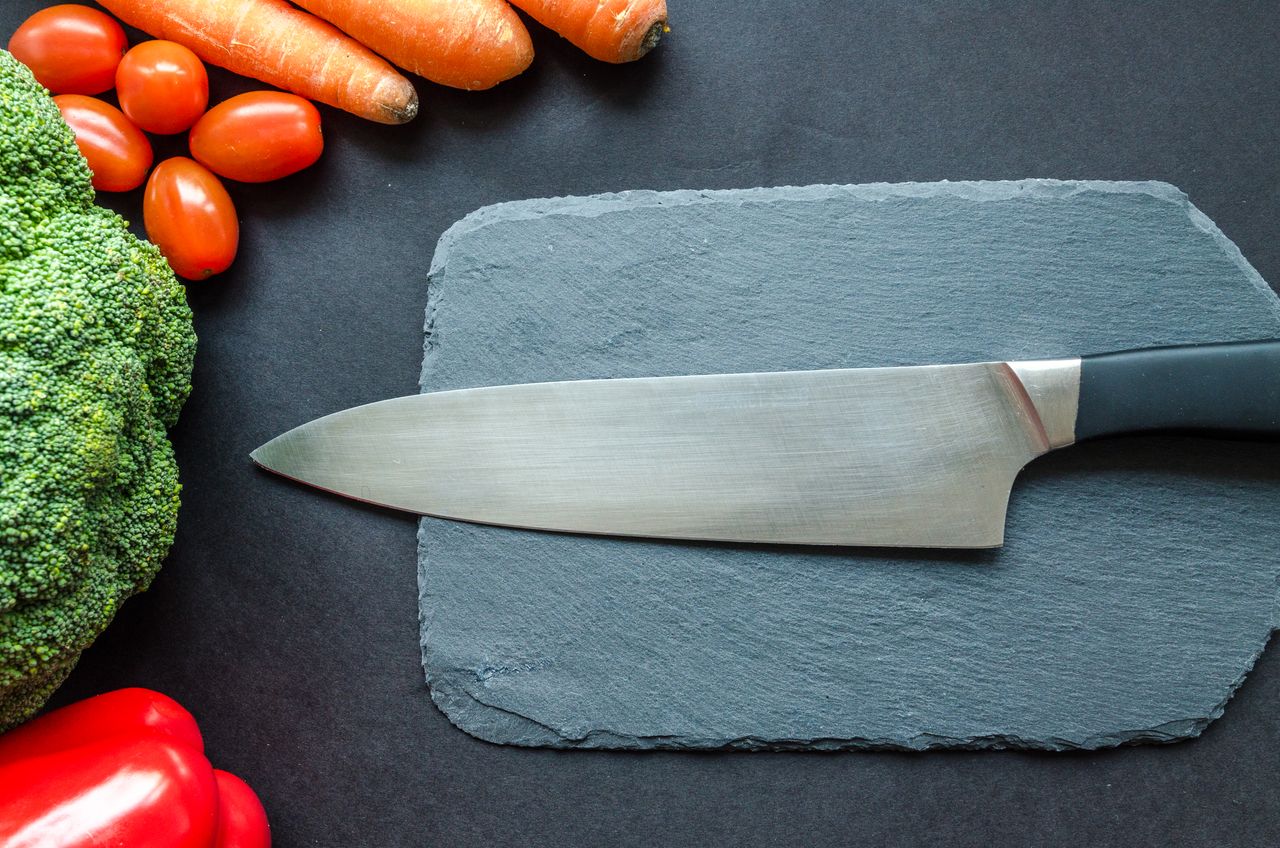 A chef's knife laid flat on a slate board with the whole blade visible from tip to heel