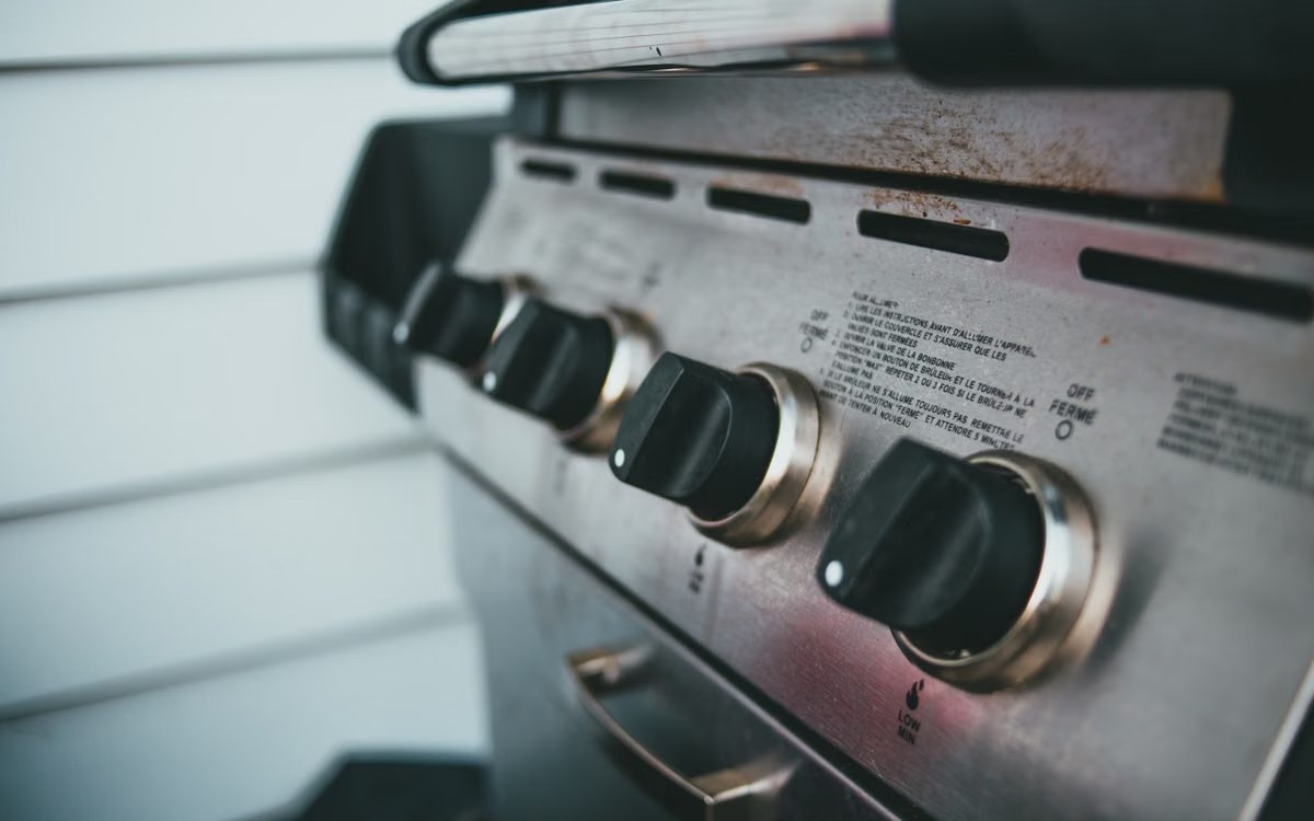 Close-up of a gas grill control panel with burner knobs and lighting instructions printed on the fascia