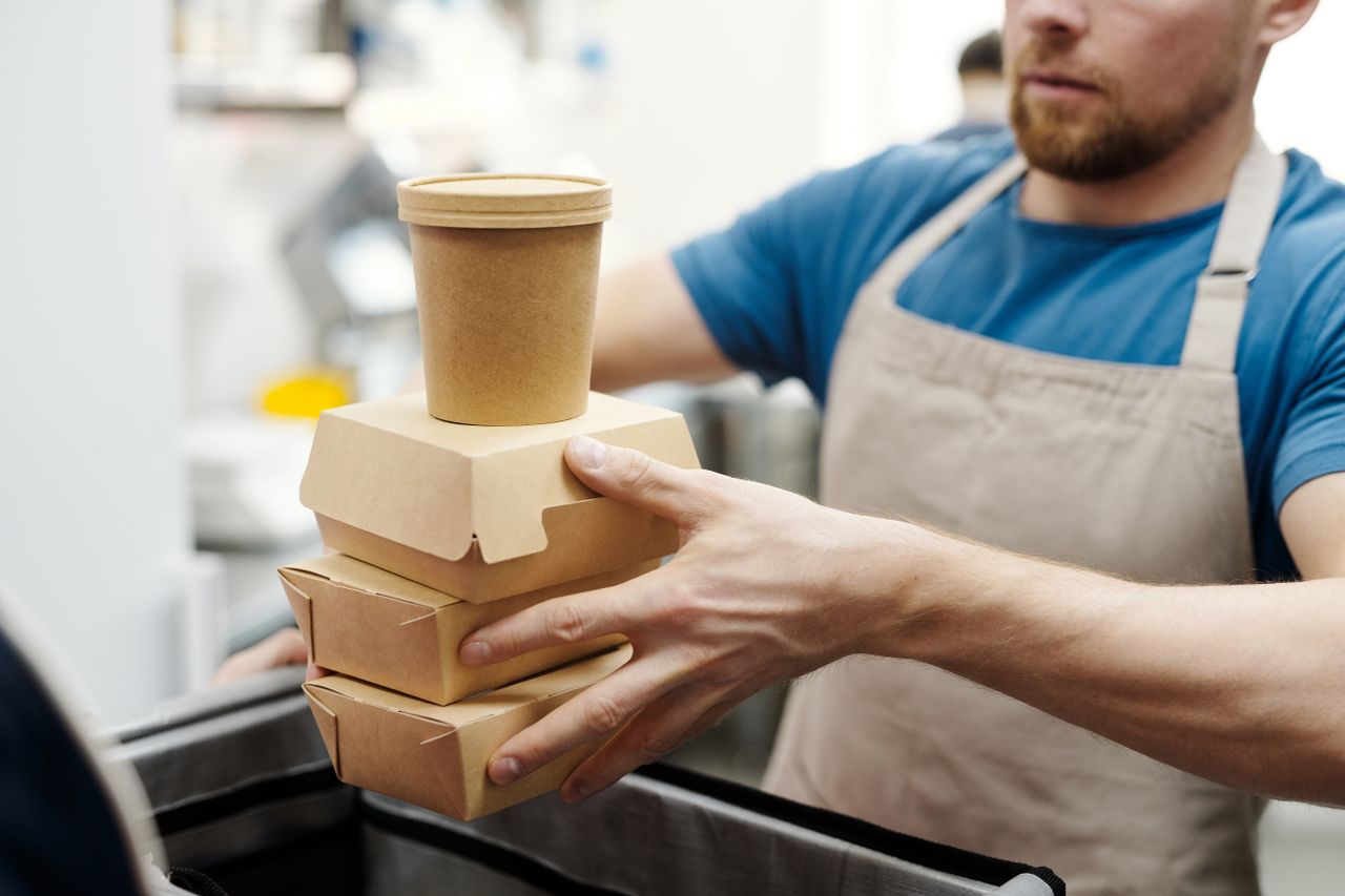 A stack of kraft cardboard takeaway containers and a paperboard soup cup held in a kitchen