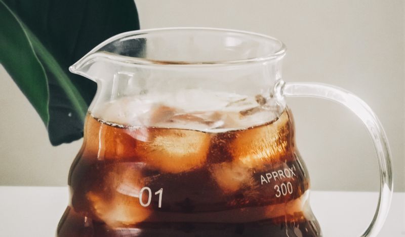 A clear glass pitcher of iced coffee with ice cubes