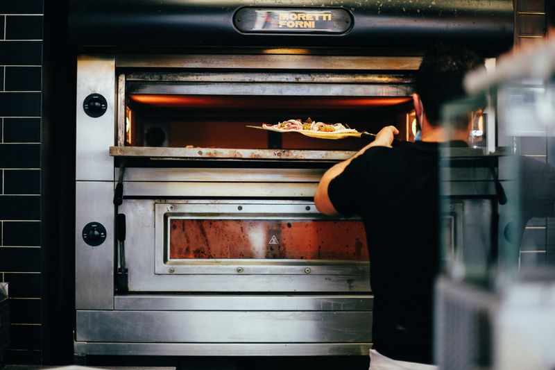 Cook sliding a pizza on a peel into an indoor electric deck oven