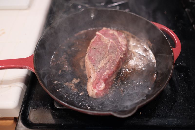Steak searing in a cast iron skillet on a stove