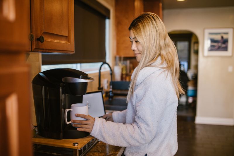 Woman using a single-serve pod coffee maker on a kitchen counter